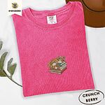 Crunchberry Comfort Colors T-shirt embroidered with an orange tabby cat asleep on a stack of green, brown and rust red books