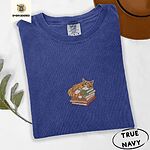 True Navy Comfort Colors T-shirt embroidered with an orange tabby cat asleep on a stack of green, brown and rust red books