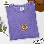 Violet Comfort Colors T-shirt embroidered with an orange tabby cat asleep on a stack of green, brown and rust red books