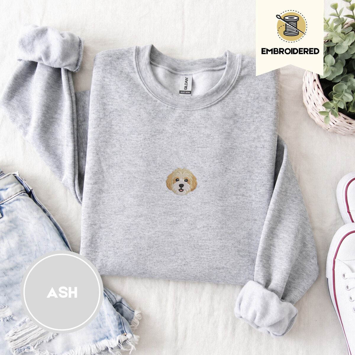 Cavachon Sweatshirt – Ash Ash crewneck sweatshirt folded with denim shorts, white sneakers and a potted plant, embroidered with a mini Cavachon face in cream and apricot with a white muzzle