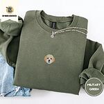 Military Green crewneck sweatshirt folded with light jeans and a silver chain necklace, embroidered with a mini Cavachon face in cream and apricot with a white muzzle