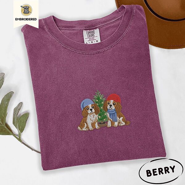 Berry Comfort Colors T-shirt embroidered with two Blenheim Cavalier King Charles Spaniels in knit beanies beside a little lit Christmas tree