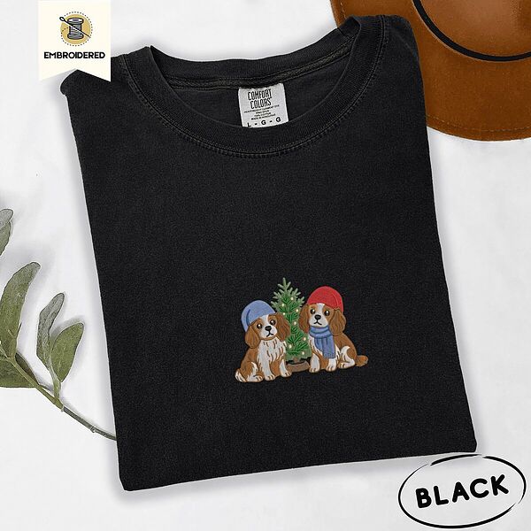 Black Comfort Colors T-shirt embroidered with two Blenheim Cavalier King Charles Spaniels in knit beanies beside a little lit Christmas tree