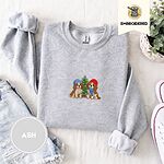 Ash crewneck sweatshirt folded with denim shorts, white sneakers and a potted plant, embroidered with two Cavalier King Charles Spaniels in knit beanies beside a little lit Christmas tree