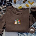 Dark Chocolate crewneck sweatshirt on a plaid flannel shirt with yellow autumn leaves and denim shorts, embroidered with two Cavalier King Charles Spaniels in knit beanies beside a little lit Christmas tree