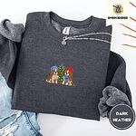 Dark Heather crewneck sweatshirt folded with ripped jeans and a silver chain necklace, embroidered with two Cavalier King Charles Spaniels in knit beanies beside a little lit Christmas tree