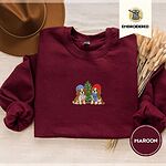 Maroon crewneck sweatshirt with a brown felt hat and dried bunny tail grass, embroidered with two Cavalier King Charles Spaniels in knit beanies beside a little lit Christmas tree