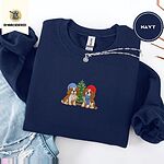 Navy crewneck sweatshirt folded with ripped jeans and a silver chain necklace, embroidered with two Cavalier King Charles Spaniels in knit beanies beside a little lit Christmas tree