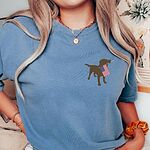 Woman in a Blue Jean T-shirt with a small chocolate lab silhouette and USA flag stitched on the left chest