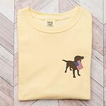 Butter yellow T-shirt laid on a wood floor with a chocolate lab carrying an American flag on the left chest