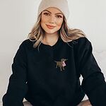 Woman in a beanie wearing a Black crewneck sweatshirt with a small chocolate lab carrying a flag on the left chest
