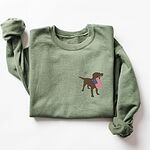 Military Green crewneck sweatshirt laid flat, embroidered with a brown Labrador holding a stars-and-stripes flag on the left chest