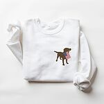 White crewneck sweatshirt laid flat, embroidered with a chocolate lab holding a red, white and blue flag on the left chest