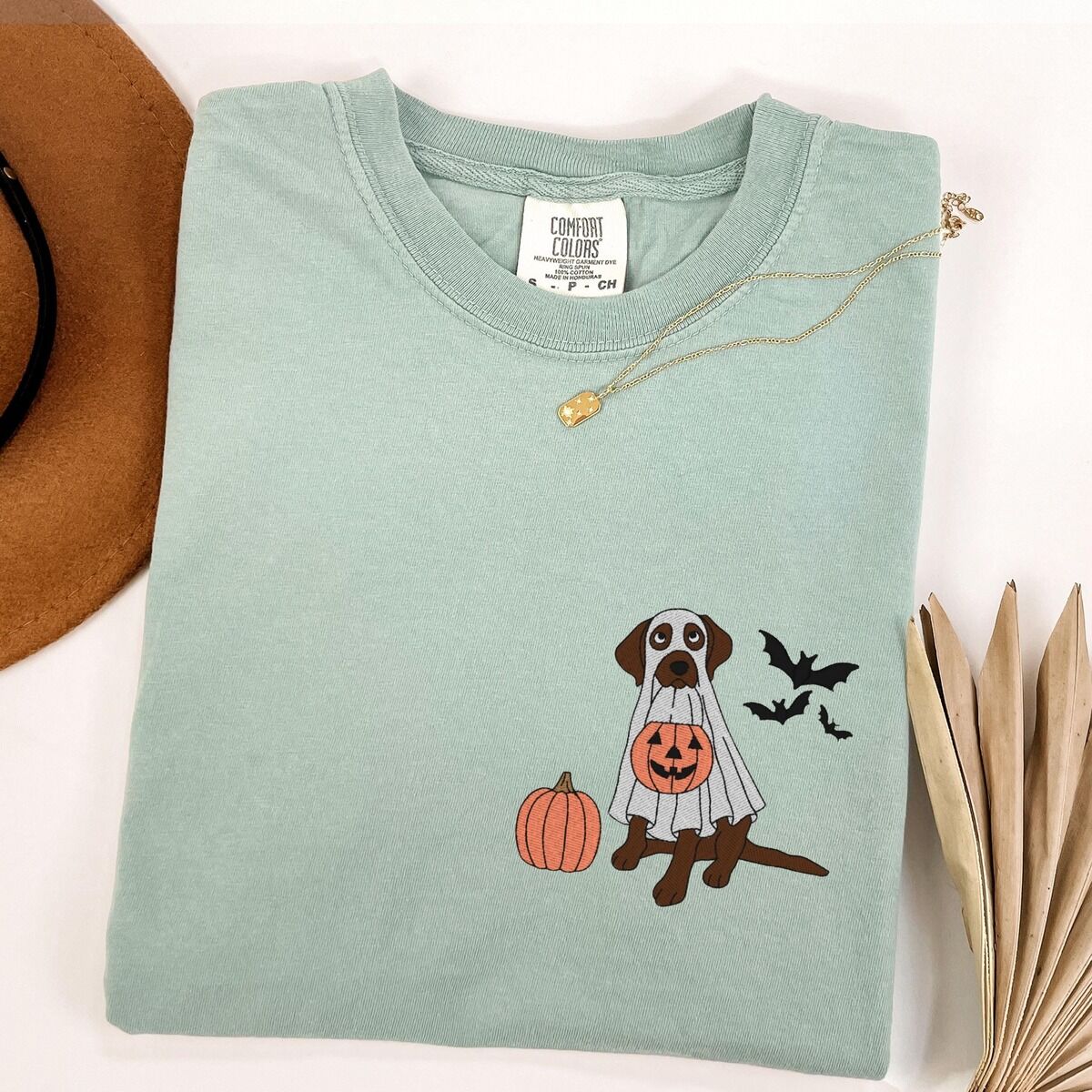 Chocolate Lab Ghost Shirt – Bay Bay T-shirt laid flat with a necklace and dried palm leaves, embroidered with a brown Labrador trick-or-treating in a ghost sheet