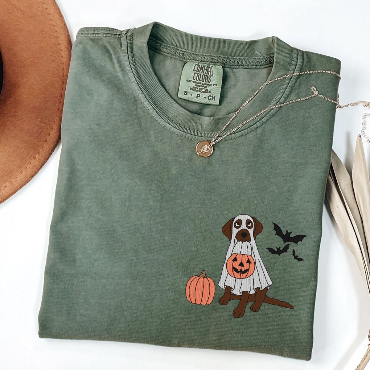 Chocolate Lab Ghost Shirt – Moss Moss T-shirt laid flat with a necklace, embroidered with a chocolate lab under a ghost sheet with a jack-o'-lantern bucket and bats