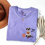 Chocolate lab ghost shirt in Violet laid flat with a necklace and a felt hat, embroidered with a brown Labrador in a ghost sheet holding a jack-o'-lantern bucket beside a pumpkin and three bats