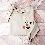 Sand crewneck sweatshirt on a wood floor, embroidered with a brown lab under a ghost sheet with a jack-o'-lantern bucket on the left chest