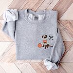 Sport Grey crewneck sweatshirt on a herringbone wood floor, embroidered with a brown lab in a ghost sheet holding a jack-o'-lantern bucket beside three bats