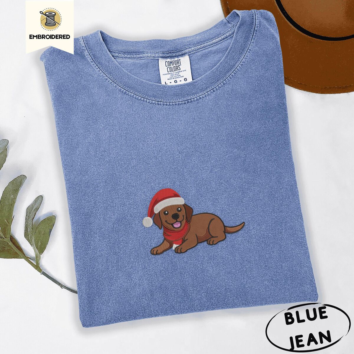 Chocolate Lab Santa Hat Shirt – Blue Jean Blue Jean Comfort Colors T-shirt embroidered with a chocolate Labrador puppy lying down in a red Santa hat and a red knit scarf