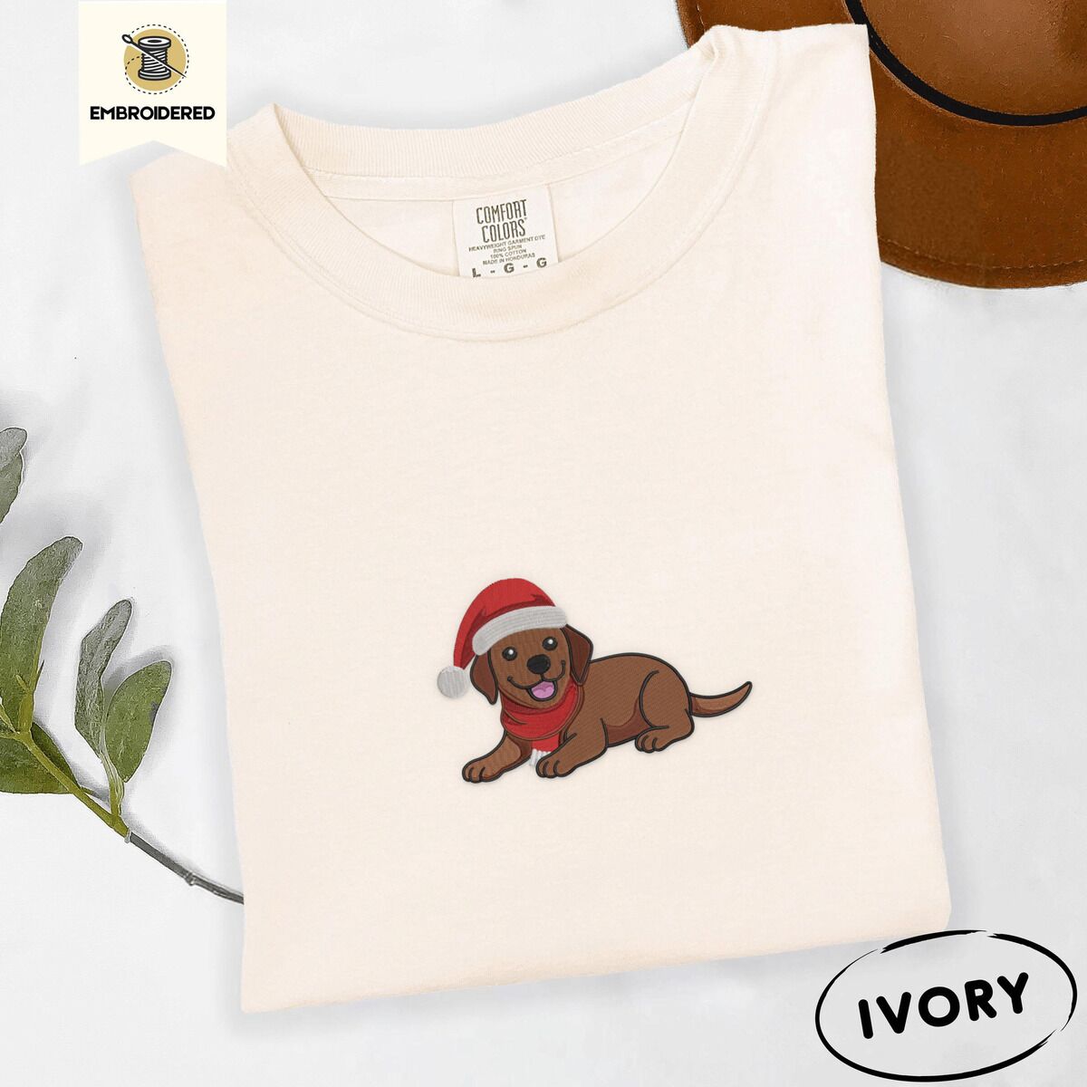 Chocolate Lab Santa Hat Shirt – Ivory Ivory Comfort Colors T-shirt embroidered with a chocolate Labrador puppy lying down in a red Santa hat and a red knit scarf