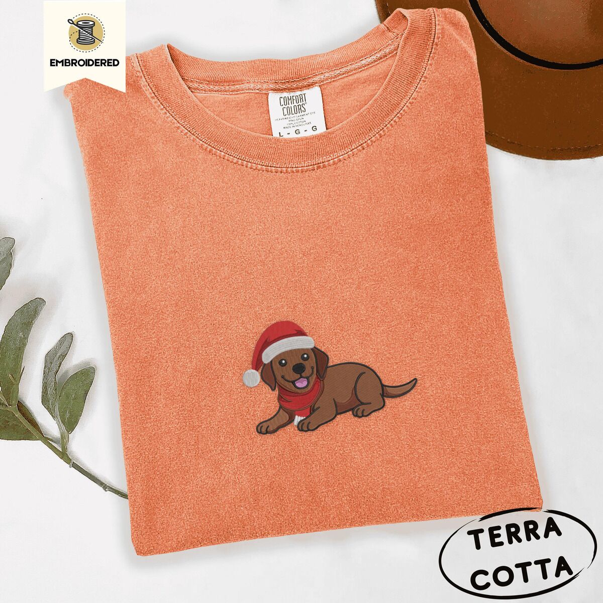 Chocolate Lab Santa Hat Shirt – Terracotta Terracotta Comfort Colors T-shirt embroidered with a chocolate Labrador puppy lying down in a red Santa hat and a red knit scarf