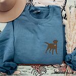 Indigo Blue crewneck sweatshirt laid flat with a hat and pampas grass, embroidered with a small chocolate brown Labrador silhouette in a blue collar and gold bone tag on the left chest