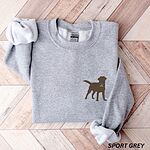 Sport Grey crewneck sweatshirt laid flat on herringbone wood, embroidered with a small chocolate brown Labrador silhouette in a blue collar and gold bone tag on the left chest