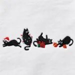 Close-up of the embroidered black cats with a Santa hat, colorful Christmas lights, a green gift box and red and gold ornaments
