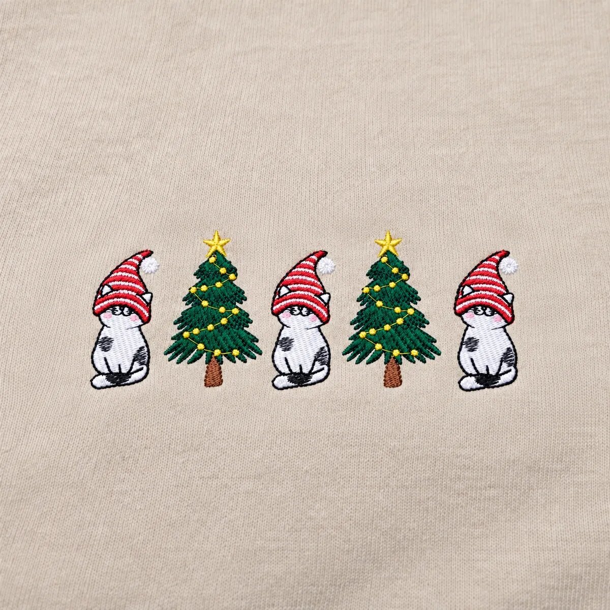 Christmas Cats in Gnome Hats Embroidery Close-up Close-up of the embroidered cats in red-and-white gnome hats between two Christmas trees with yellow lights and stars