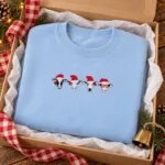 Light blue Christmas cow sweatshirt folded in a kraft gift box with a buffalo check ribbon and a cow bell