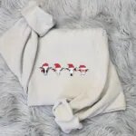 Christmas cow sweatshirt in Sand with four embroidered cow heads in red Santa hats, one with red bows and one in red sunglasses