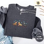 Dark Heather crewneck sweatshirt folded with ripped jeans and a silver chain necklace, embroidered with three horses in Santa hats, a red scarf and red leg wraps under turquoise snowflakes