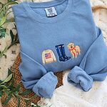 Blue Jean Comfort Colors crewneck sweatshirt with rolled cuffs on a woven bag, embroidered with a tan flag sweater, navy rain boots and a golden retriever in a red bow