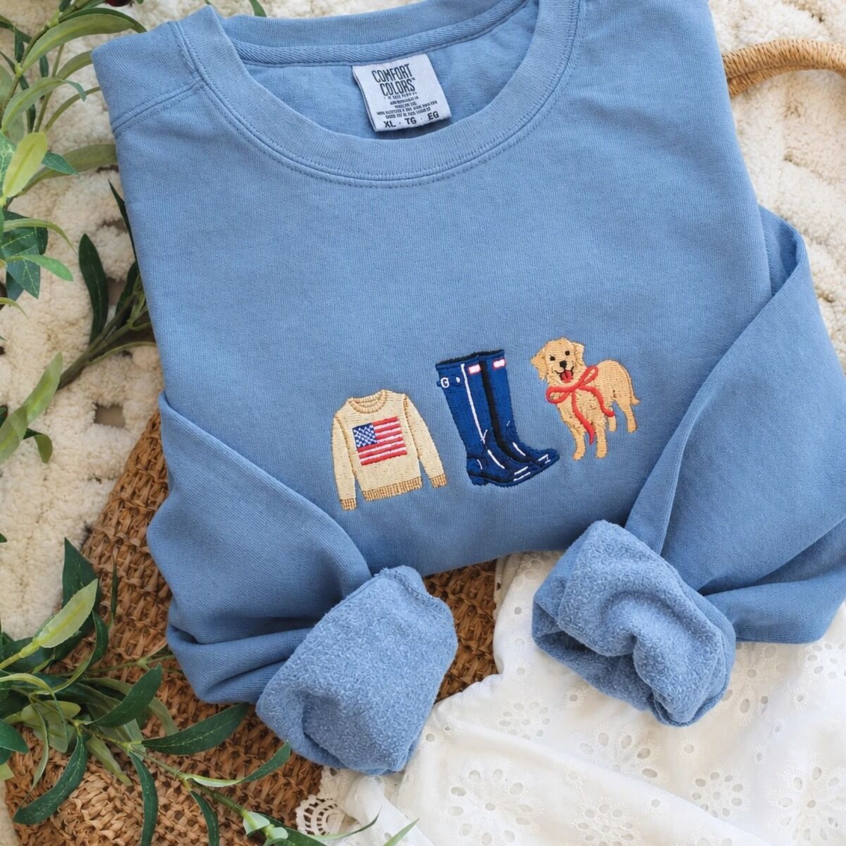 Coastal Icons Sweatshirt – Blue Jean Blue Jean Comfort Colors crewneck sweatshirt with rolled cuffs on a woven bag, embroidered with a tan flag sweater, navy rain boots and a golden retriever in a red bow