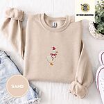 Sand crewneck sweatshirt folded with denim shorts, white sneakers and a potted plant, embroidered with a white goose in a Santa hat and a red ribbon bow in the center of the chest