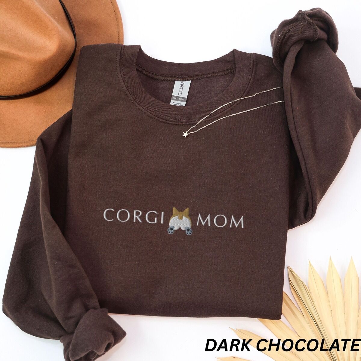 Corgi Butt Sweatshirt – Dark Chocolate Dark Chocolate crewneck sweatshirt laid flat with a felt hat and a necklace, embroidered with CORGI MOM and a fluffy corgi rear with two paws