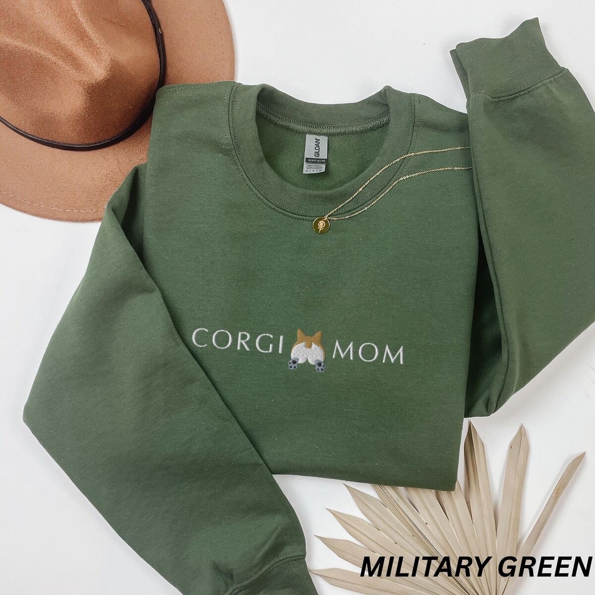 Corgi Butt Sweatshirt – Military Green Military Green crewneck sweatshirt laid flat with a felt hat and dried palm leaves, embroidered with CORGI MOM and a corgi butt