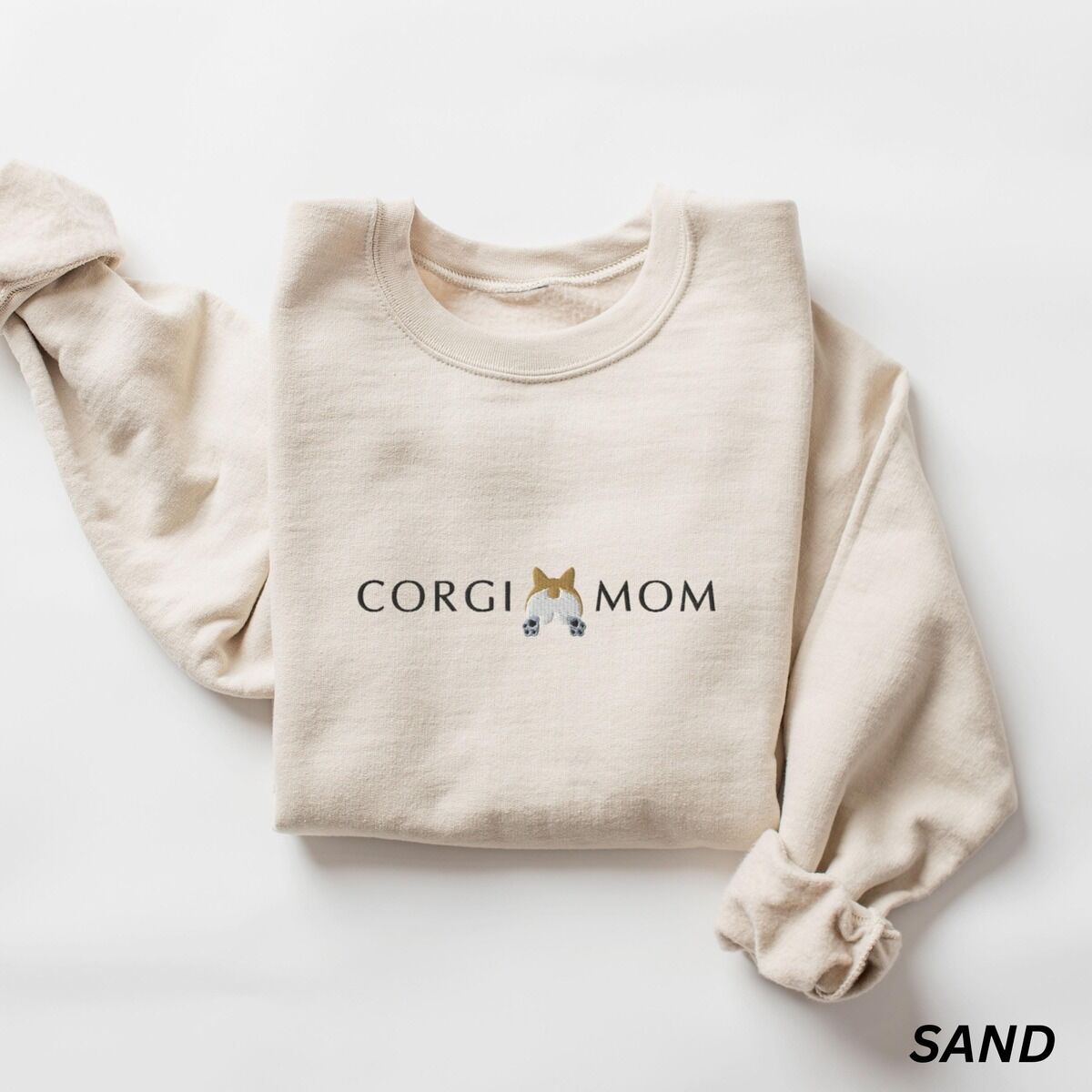 Corgi Butt Sweatshirt – Sand Sand corgi butt sweatshirt laid flat on white, embroidered with CORGI MOM and a fluffy white and tan corgi butt between the words