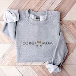 Sport Grey crewneck sweatshirt laid flat on herringbone wood, embroidered with CORGI MOM and a white and tan corgi butt