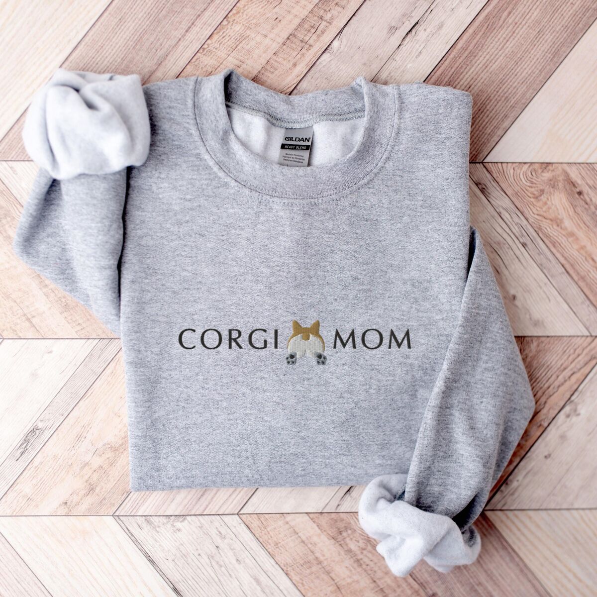 Corgi Butt Sweatshirt - Sport Grey Sport Grey crewneck sweatshirt laid flat on herringbone wood, embroidered with CORGI MOM and a white and tan corgi butt