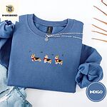 Indigo Blue crewneck sweatshirt folded with light jeans and dried twigs, embroidered with three tricolor corgis in red knit scarves among sprigs of holly