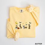 Butter crewneck sweatshirt laid flat with a knotted sleeve, embroidered with four corgis under a crescent moon with bats, gold sparkles and a jack-o'-lantern