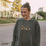 Woman wearing a Pepper crewneck sweatshirt on a tree-lined street, a wider view, embroidered with four corgis under a crescent moon with bats, gold sparkles and a jack-o'-lantern
