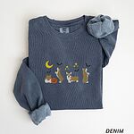 Denim crewneck sweatshirt laid flat with a rolled sleeve, embroidered with four corgis under a crescent moon with bats, gold sparkles and a jack-o'-lantern