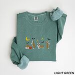 Light Green crewneck sweatshirt laid flat with rolled sleeves, embroidered with four corgis under a crescent moon with bats, gold sparkles and a jack-o'-lantern