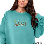 Woman wearing a Seafoam crewneck sweatshirt, embroidered with four corgis under a crescent moon with bats, gold sparkles and a jack-o'-lantern