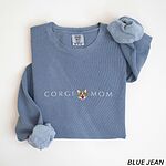 Blue Jean crewneck sweatshirt laid flat on white, embroidered with CORGI MOM in light thread around a smiling corgi face