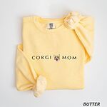 Butter crewneck sweatshirt laid flat on white, embroidered with CORGI MOM in dark thread and a red and white corgi face with its tongue out