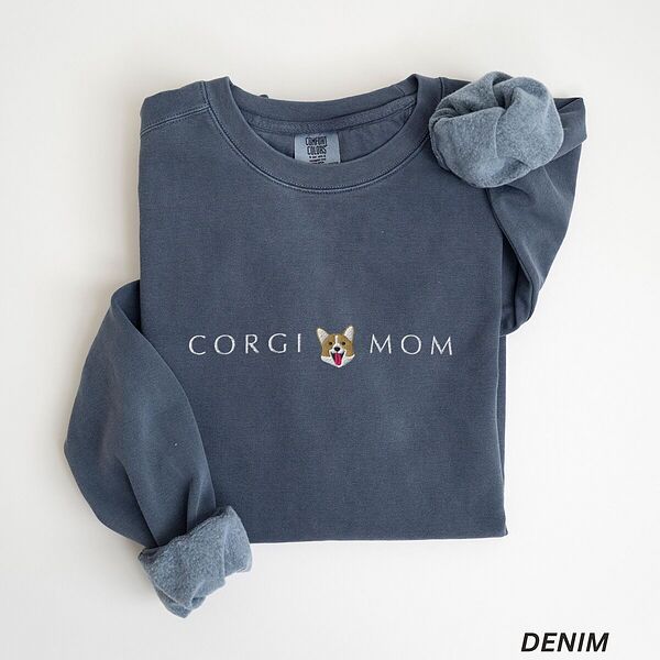Denim corgi mom sweatshirt laid flat on white with a rolled cuff, embroidered with CORGI MOM and a smiling corgi face between the words