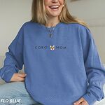 Smiling woman in a Flo Blue crewneck sweatshirt embroidered with CORGI MOM and a red and white corgi face